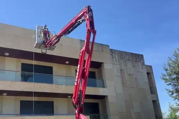 Nacelle élévatrice rouge déployée le long de la façade en pierre d'un immeuble de bureaux