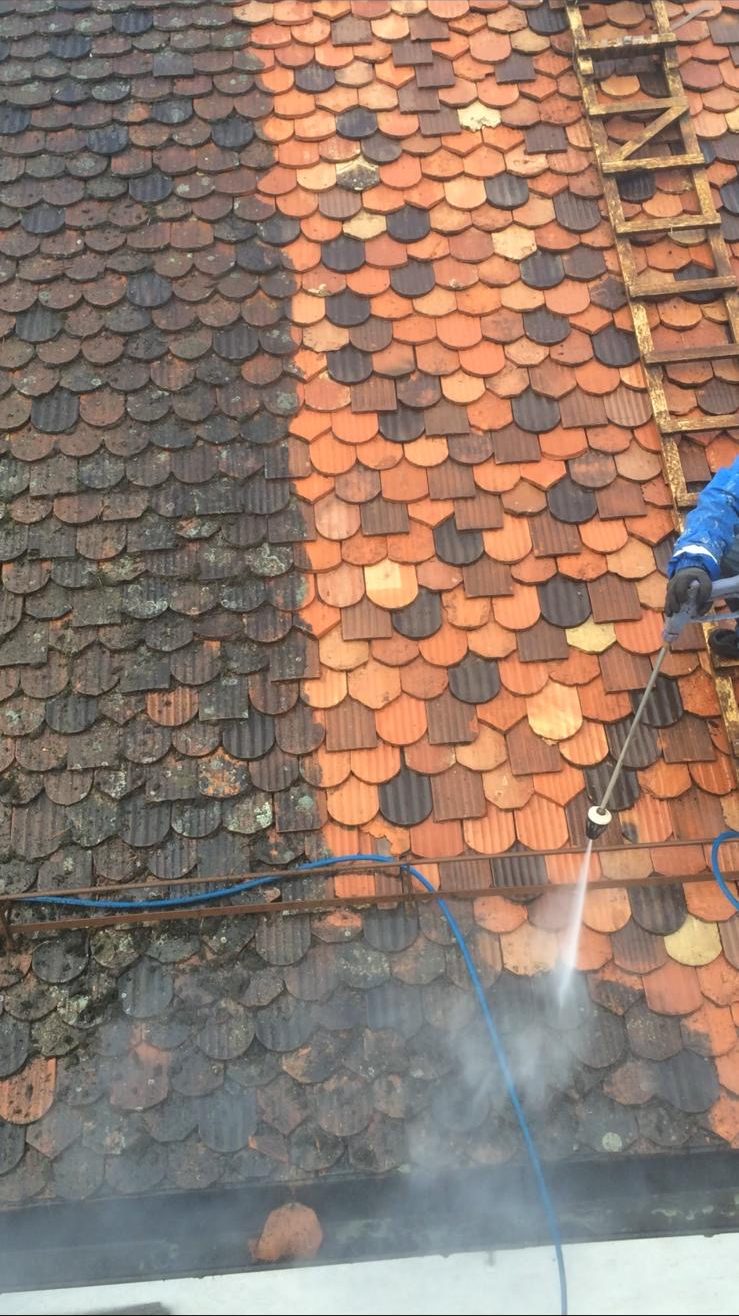 Toiture en tuiles écaille en cours de nettoyage haute pression : à gauche les mousses et le noircissement, à droite la terre cuite orangée retrouvée